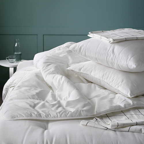 Cama con edredón blanco y almohadas, pared verde. Materiales suaves, esponjosos, ligeros y cálidos, reciclados.