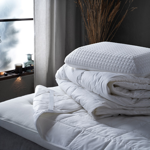 Un acogedor edredón blanco colocado sobre una cama, con almohadas blancas suaves y esponjosas y mantas dobladas, con una ventana al fondo.