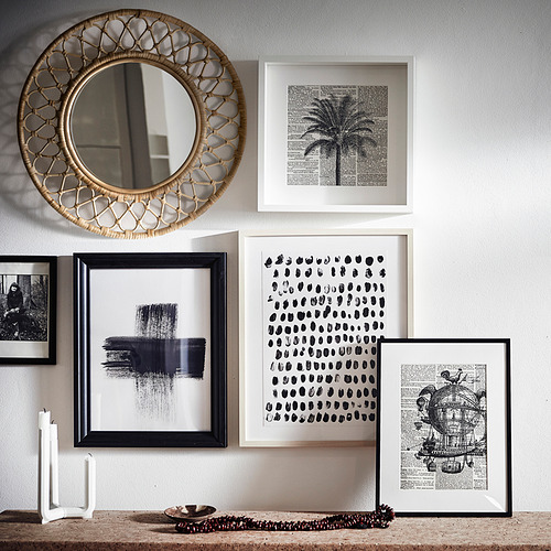 Espejo de ratán GRINSBOL rodeado de obras de arte enmarcadas en blanco y negro, creando una composición vibrante y texturizada.