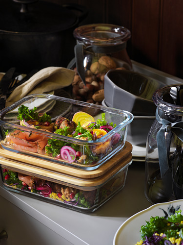 En el interior hay recipientes de vidrio para preparar comidas con tapas de madera, llenos de verduras de colores. Detrás, hay frascos y tazas en un mostrador.