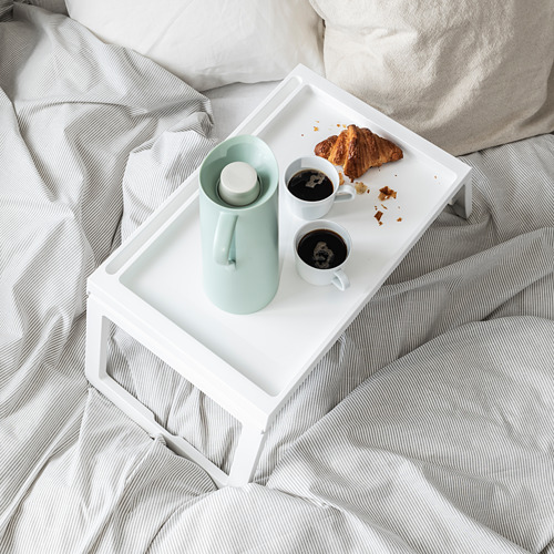 Una bandeja de cama blanca KLIPSK con un termo verde, dos tazas de café y un croissant sobre una colcha a rayas.