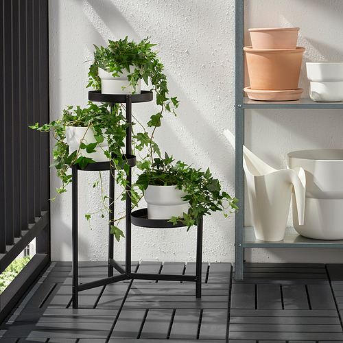 El soporte de plantas de tres niveles muestra plantas verdes en un balcón, utilizando el espacio vertical de manera eficiente.