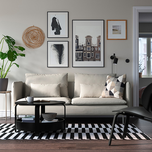Salón moderno con sofá SÖDERHAMN blanco, cojines grises, mesa de centro negra, alfombra de rayas y pared de galería. El sofá encaja bien con los elementos circundantes.