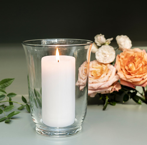 Candelabro de cristal transparente con vela blanca y rosas rosas.