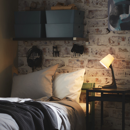 Acogedor dormitorio con pared de ladrillo visto, cama con almohadas blancas, mesita de noche, lámpara y estantes de pared.