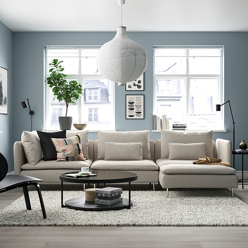 Moderna sala de estar azul con un gran sofá seccional SÖDERHAMN beige, almohadas de colores, mesa de café redonda, grandes ventanales y lámpara colgante.