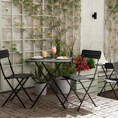 Juego de mesa de exterior de metal negro con dos sillas, flores, vasos y platos. Perfecto para espacios pequeños.