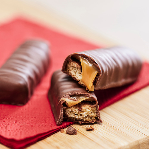 Dos tabletas de chocolate sobre pañuelo rojo. Uno es mordido, revelando un caramelo crujiente y masticable y un chocolate suave.