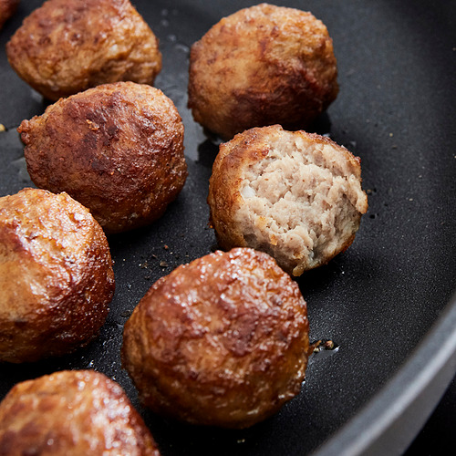 La imagen muestra siete albóndigas marrones fritas en una sartén. Uno está cortado por la mitad, revelando el interior.