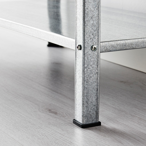 La imagen muestra un primer plano de una robusta pata de estante de metal galvanizado sobre un piso de madera. La pata ajustable pies de plástico negro para la protección del suelo.