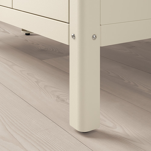 Primer plano de la pata de un armario de metal blanco con patas ajustables sobre un suelo de madera.