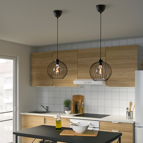 Cocina moderna con gabinetes de madera, encimera negra, lámparas colgantes, tabla de cortar, fregadero, estufa, nevera, hierba en maceta.