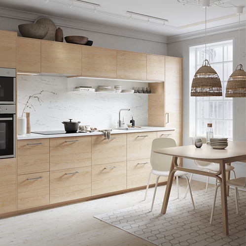Cocina moderna con gabinetes de madera clara, protector contra salpicaduras de mármol, mesa blanca y lámparas colgantes de mimbre.