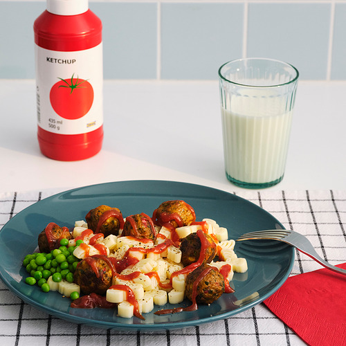 Una comida con guisantes, patatas, salchichas, ketchup, leche, sobre un mantel a cuadros.