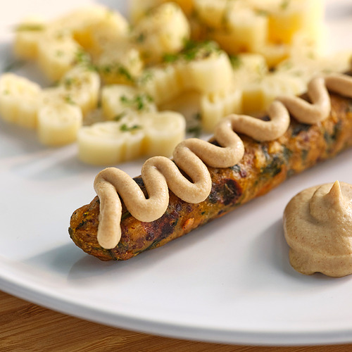 El plato blanco contiene salchicha marrón rociada con salsa cremosa, junto a ensalada de papa dorada.