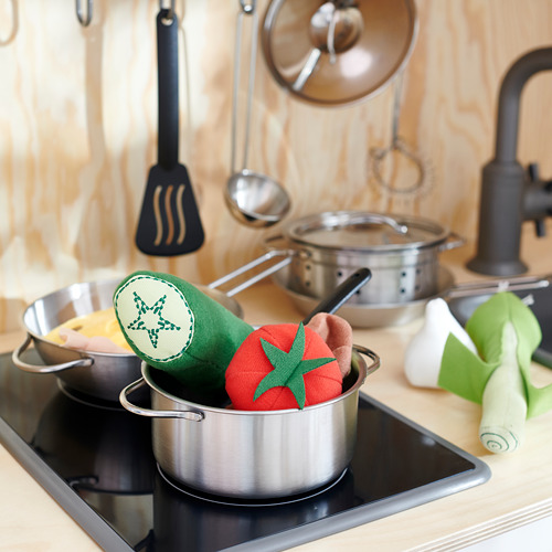 Los niños juegan a la cocina con ollas de metal, manoplas verdes, rojas y beige. Fondo de madera, utensilios para colgar, grifo negro.