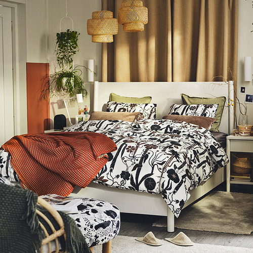 Dormitorio con edredón blanco LUNDSKAFTING, estampado botánico, manta roja, almohadas verdes, planta, lámparas, suelo de madera, cortinas grandes.