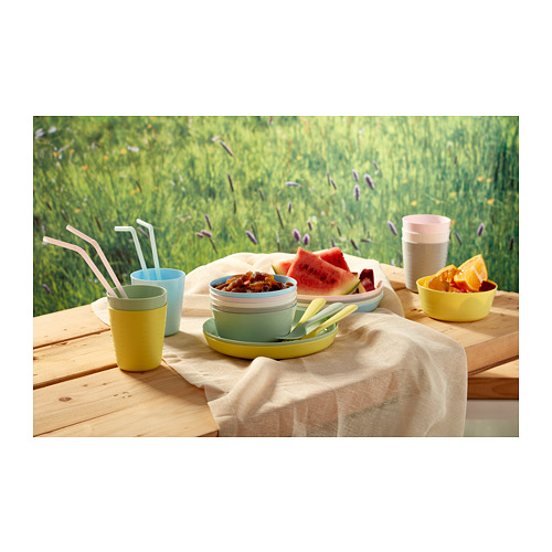 Cuencos y tazas para niños en la mesa. Incluye cucharas y pajitas, colocadas al aire libre sobre una mesa de madera con fondo verde.