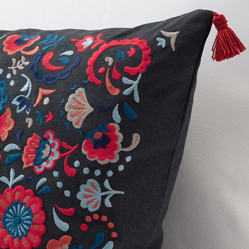Cojín bordado con flores vibrantes sobre tela oscura, detalle de borla roja.
