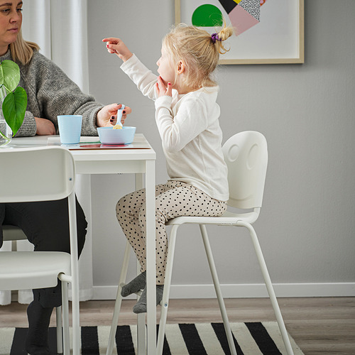 Niño sentado en la silla junior de VILDGÅS, comiendo de un cuenco azul. Mamá se sienta a su lado, con la silla apilada debajo de la mesa.