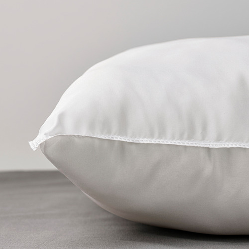 Primer plano de una almohada blanca y regordeta sobre una cama, que muestra su textura suave y sus costuras precisas.