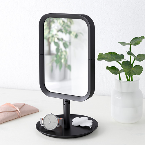 Moderno espejo de tocador con lado de aumento, colocado sobre una mesa con accesorios y una planta.