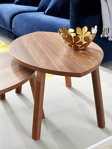 Dos mesas redondas anidadas con patas de madera cuentan con un cuenco dorado decorativo en la parte superior, colocado contra un sofá azul. Diseño escandinavo moderno y elegante.
