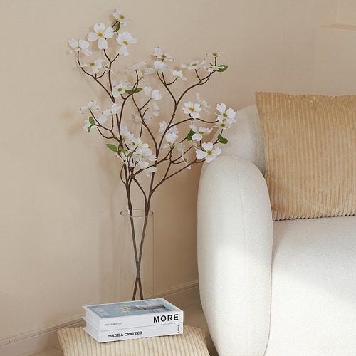 Jarrón con flores artificiales blancas junto a silla y libros.
