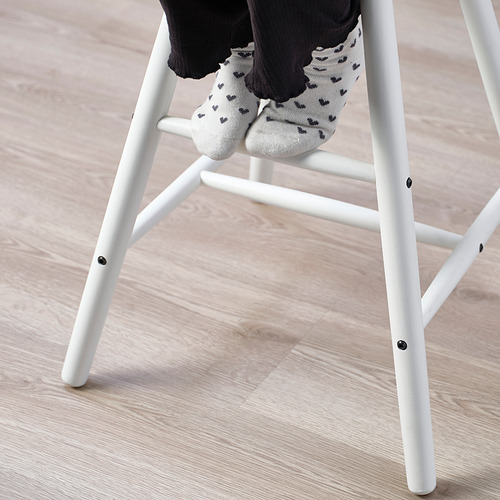 Los pies de los niños con calcetines de Mickey Mouse descansan sobre el reposapiés de la silla junior blanca, ideal para la altura de la mesa de comedor.