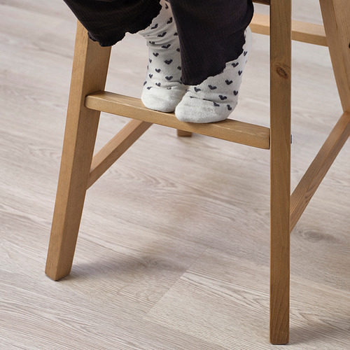 Niño sentado en una silla junior, diseñada para la altura de la mesa de comedor. La silla tiene patas de madera visibles y reposapiés para apoyo.