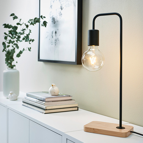 Lámpara TVÄRHAND negra minimalista sobre superficie blanca con decoración.