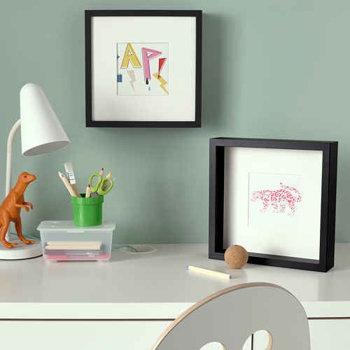 Un escritorio con una taza verde, material de oficina, dos fotos enmarcadas, una lámpara y un dinosaurio de juguete.