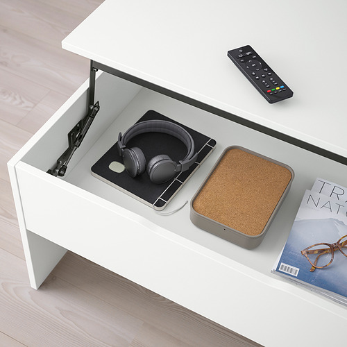 Una moderna mesa de centro ajustable con una parte superior elevable, que revela el almacenamiento que contiene auriculares y un control remoto.