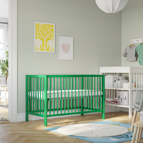 Cuna GULLIVER verde brillante, cuadrada con husos, encaja bien en una guardería acogedora, rodeada de decoración.