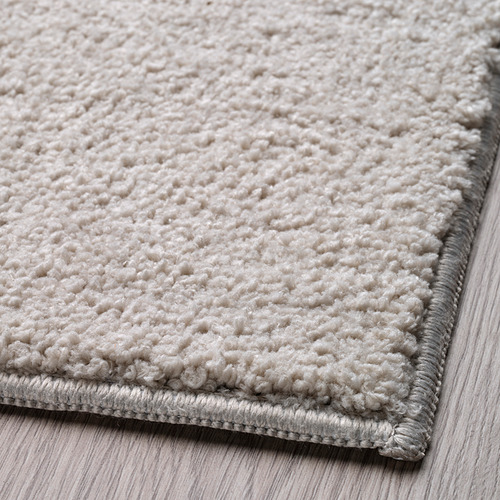 Primer plano de una alfombra beige suave y texturizada con borde gris, que muestra material de calidad y tejido intrincado.