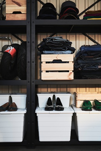 Estantes de almacenamiento BROR negros con contenedores blancos, cajas de madera y ropa doblada.