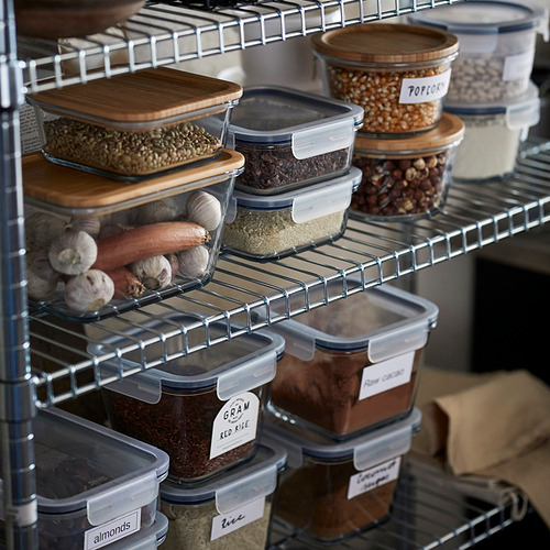 Estantes llenos de recipientes de alimentos etiquetados, algunos con tapas de madera, que almacenan varios productos secos y verduras.
