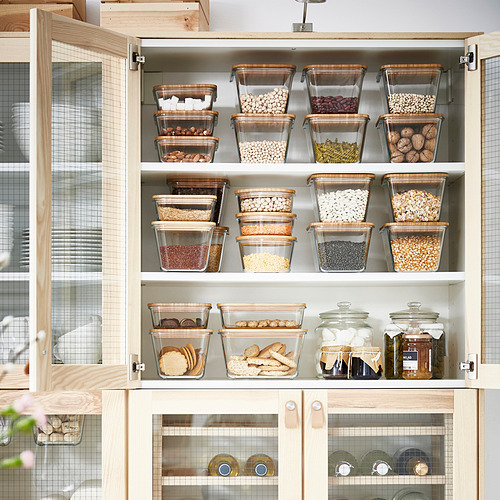 Gabinete de cocina con recipientes de vidrio para almacenar granos y bocadillos, las tapas sellan la frescura y se apilan para el uso del espacio, las tapas de madera agregan calidez.