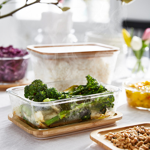 Recipiente de vidrio para alimentos con brócoli, se asienta sobre una base de bambú, sube el vapor, ideal para almacenar y calentar comidas.