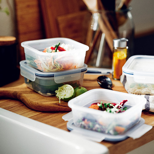 Varios recipientes de plástico para alimentos, sellables, apilados sobre una mesa de madera con rodajas de lima. Ideal para almacenar las sobras, transparente para facilitar la visibilidad.