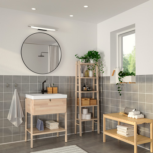 Baño moderno con espejo negro LINDBYN. Espejo redondo y grande sobre tocador de madera clara. Plantas y toallas en estanterías de madera.