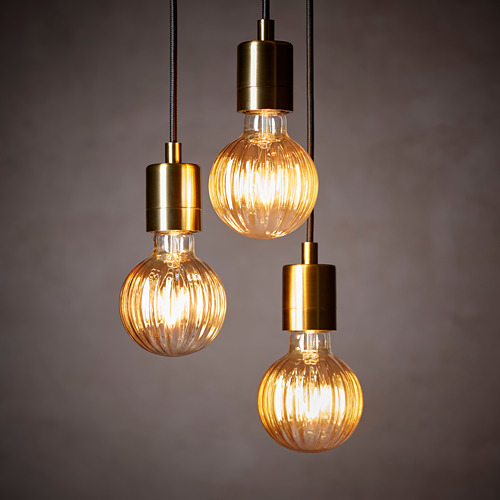 Tres modernas lámparas colgantes con bombillas de vidrio acanalado cuelgan de cordones de color dorado. Las bombillas están iluminadas, emitiendo un resplandor cálido.