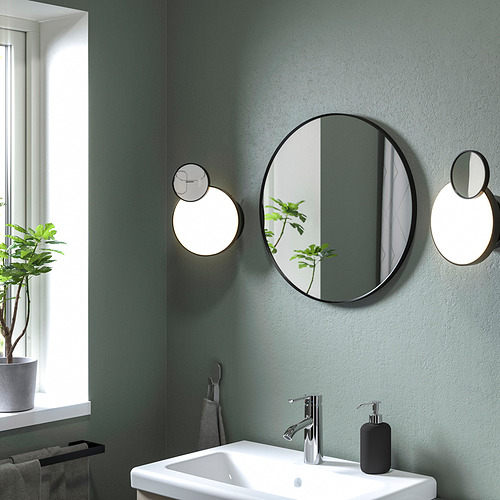 Baño moderno con espejo redondo LINDBYN, lavabo blanco y planta verde.