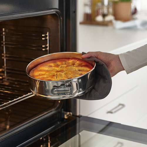 Persona que usa guantes de cocina para sacar un plato horneado de color marrón dorado de un horno. La bandeja desmontable de acero inoxidable garantiza una distribución uniforme del calor.