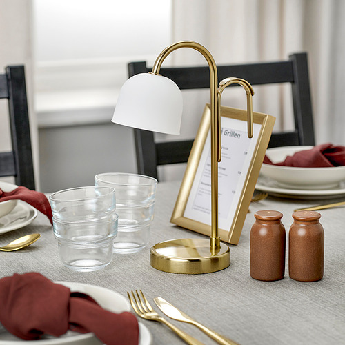 Una elegante lámpara portátil sobre una mesa, que se ilumina con una luz blanca cálida, mostrando su base de latón y su pantalla de vidrio esmerilado.