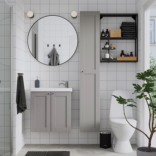 Baño moderno: espejo redondo, marco negro, tocador gris. Inodoro blanco, almacén, planta. Ducha de cristal.