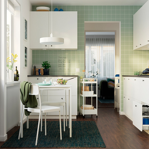 Cocina moderna con sillas blancas, piso de madera, paredes verdes, ensalada, vino, suéter.