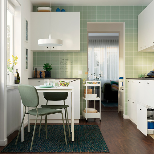 Pequeña mesa y silla verde VIHALS colocadas en un acogedor rincón de la cocina con lámpara colgante, cerca del vestíbulo de entrada.