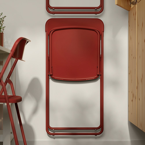 Una silla plegable roja de VIHALS apoyada contra una pared blanca. La silla se pliega, lo que demuestra su diseño que ahorra espacio.