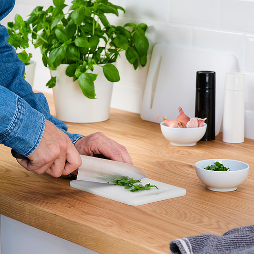 La persona corta hierbas en una tabla de cortar de plástico LEGÍTIMA, adecuada para varios alimentos y cuchillos.